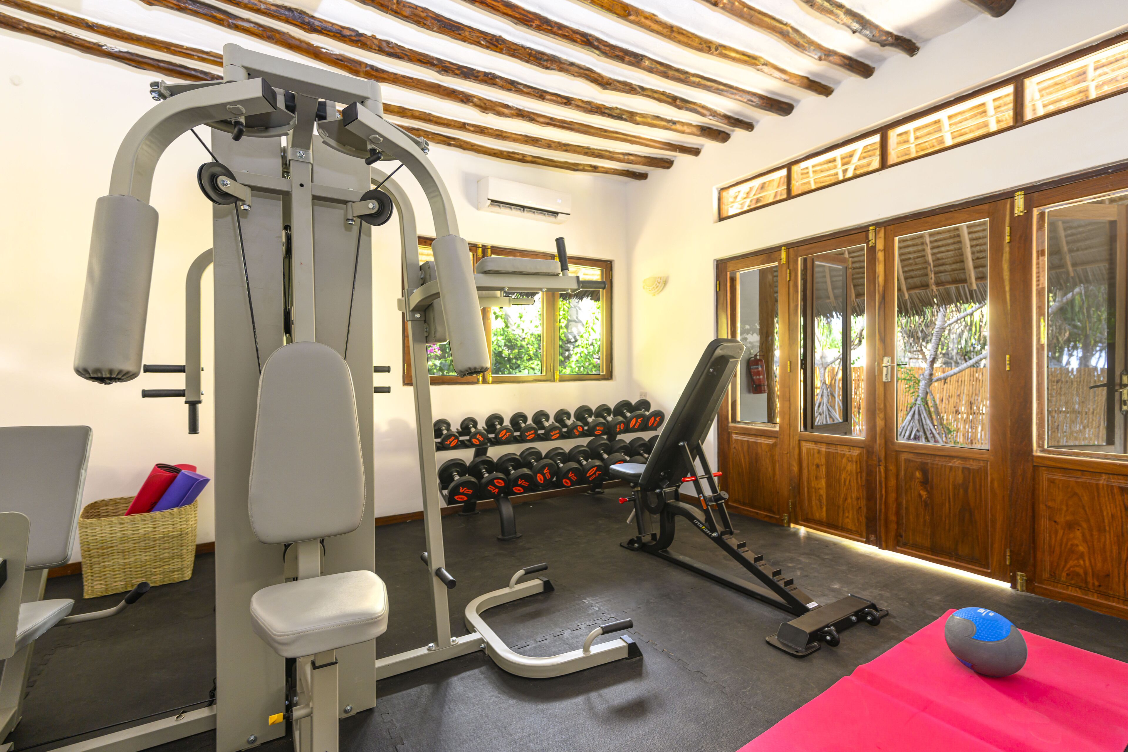 Une salle de sport équipée de matériel d’exercice, avec un tapis rouge et un panier contenant divers objets.