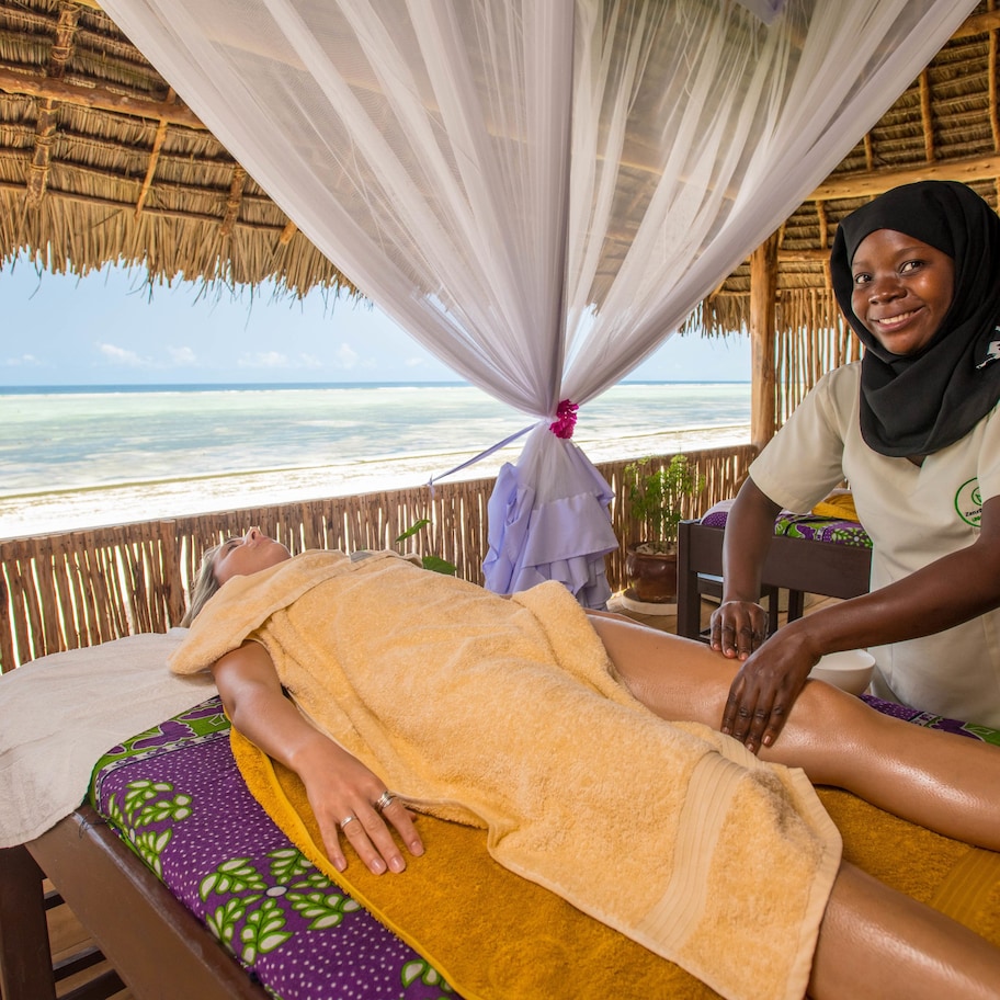 A massage therapy room with a view of the ocean, a wooden ceiling, and a bed with a colorful bedspread.