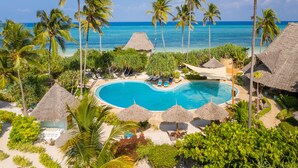 A resort with a central swimming pool, surrounded by palm trees and thatched-roof structures. - Zanzibar Queen Hotel (Matemwe)
