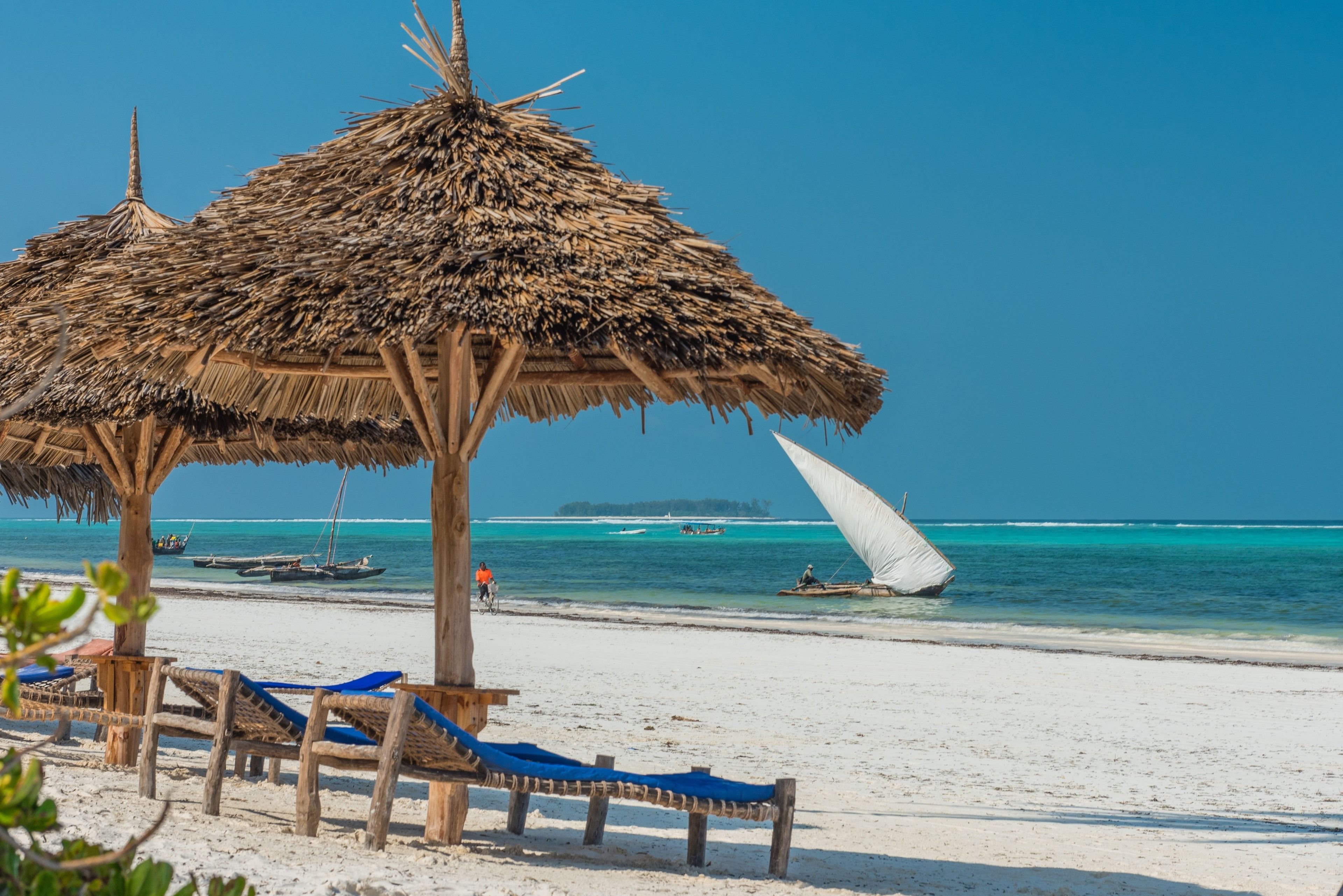A beach with thatched umbrellas and wooden lounge chairs.