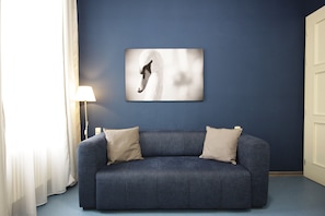 Ein Zimmer mit blauer Wand, weißer Tür und blauem Sofa mit zwei beigen Kissen.