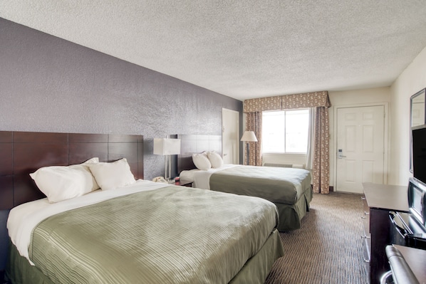A hotel room with two beds, a desk, a TV, and a window with curtains.