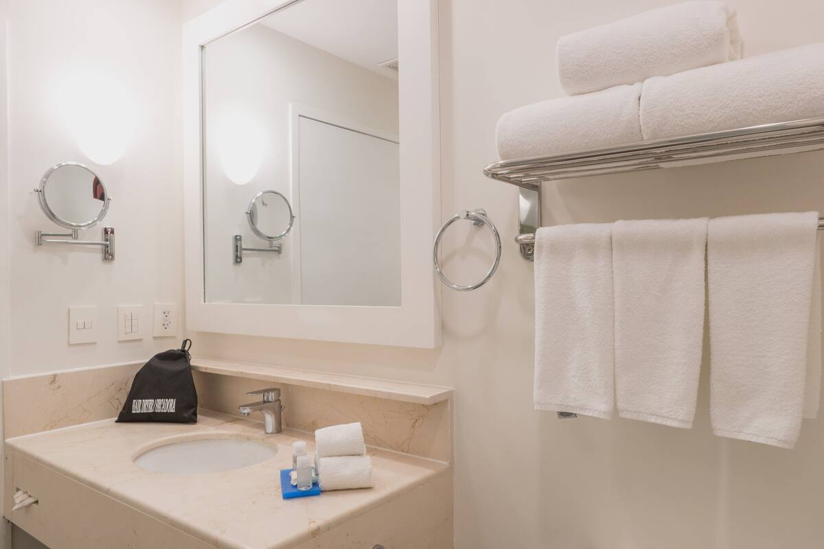 Een badkamer met een wastafel, spiegel, handdoekhouder en een zwarte tas op het aanrecht.