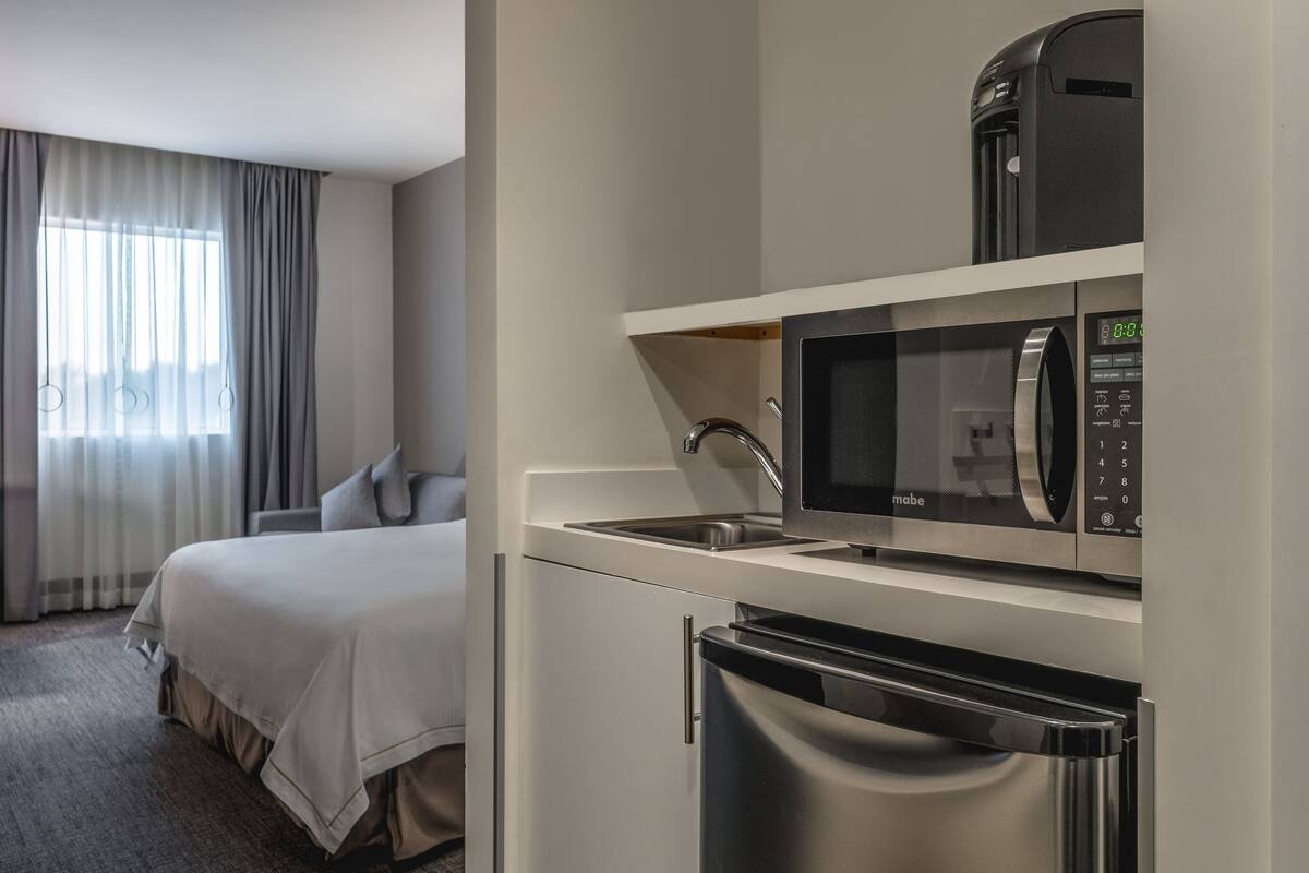 Een hotelkamer met een bed, een kitchenette met een magnetron, een koffiezetapparaat en een koelkast.