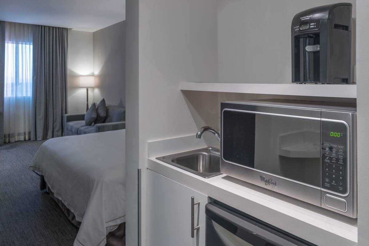 Een compacte hotelkamer met een kitchenette, inclusief een magnetron, koffiezetapparaat en spoelbak.