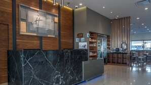 Un hall d’hôtel moderne avec un comptoir d’accueil en marbre, des éléments décoratifs en bois et un espace salon comprenant des tables et des chaises.