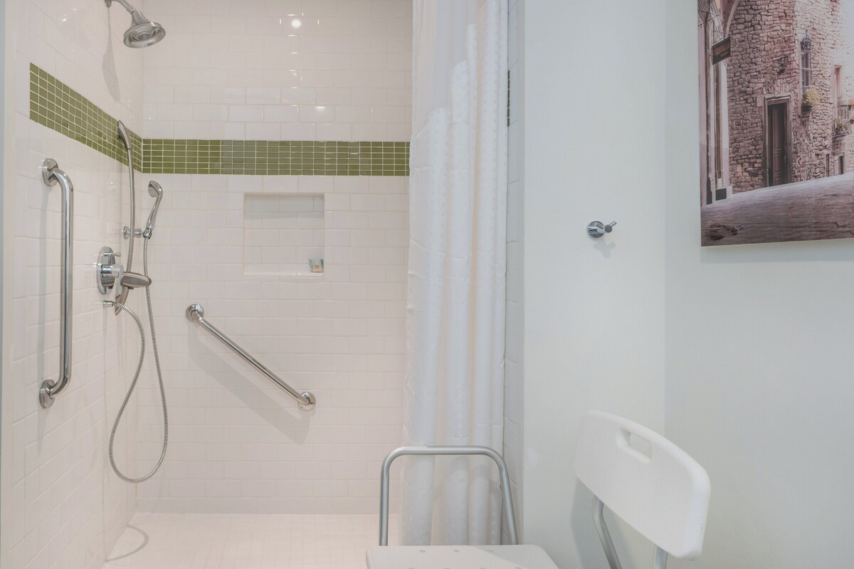Une salle de bain équipée d’une douche, de barres d’appui, de toilettes et d’un lavabo.
