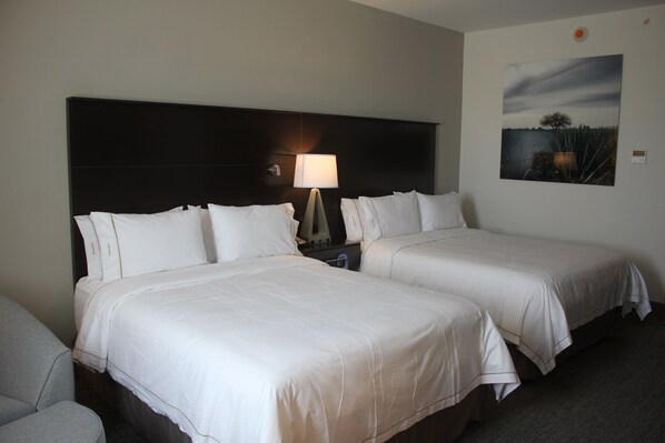 A hotel room with two beds, a nightstand, a lamp, and a painting on the wall.
