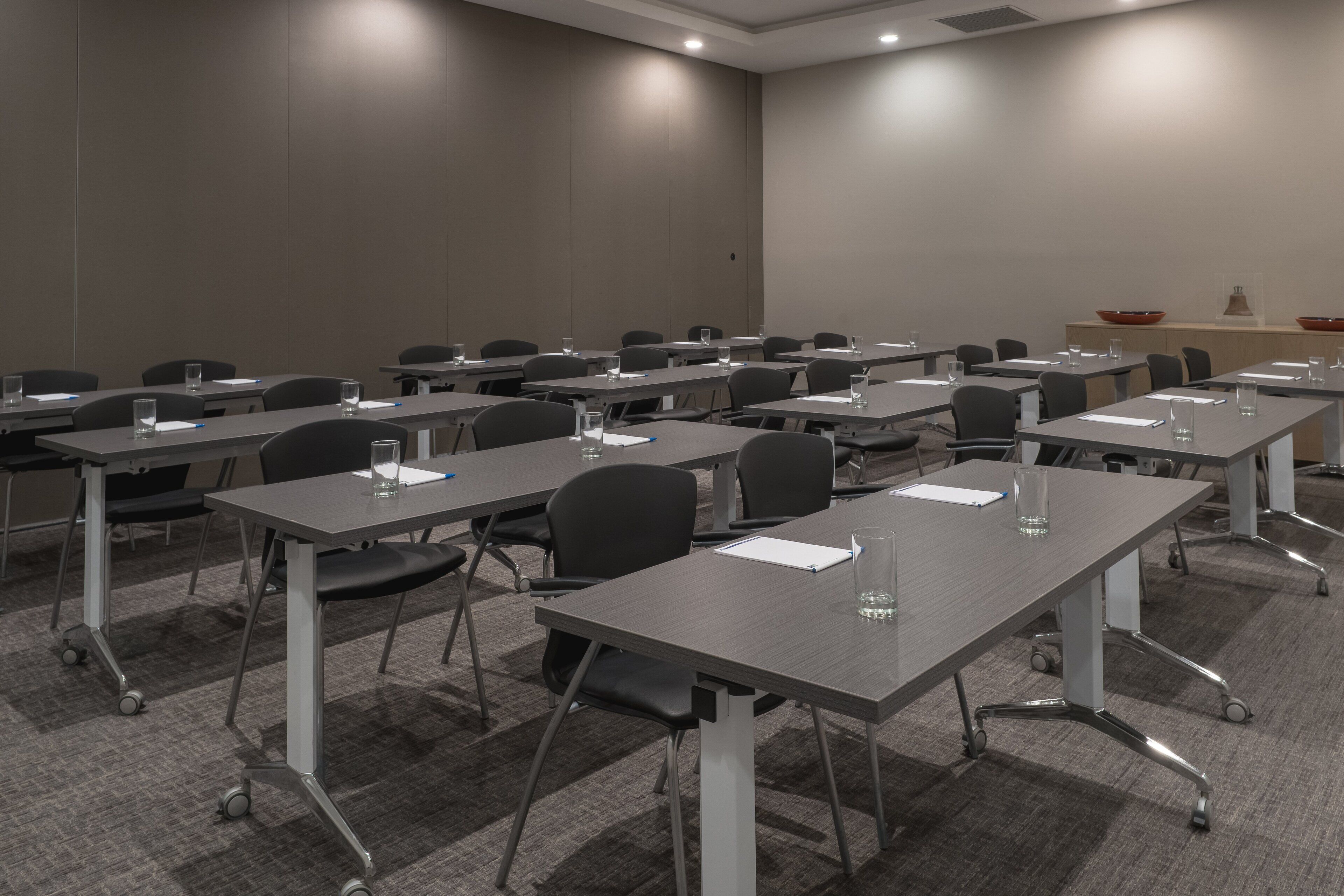 Un salón de conferencias con varias mesas y sillas, equipado con vasos de agua y documentos.