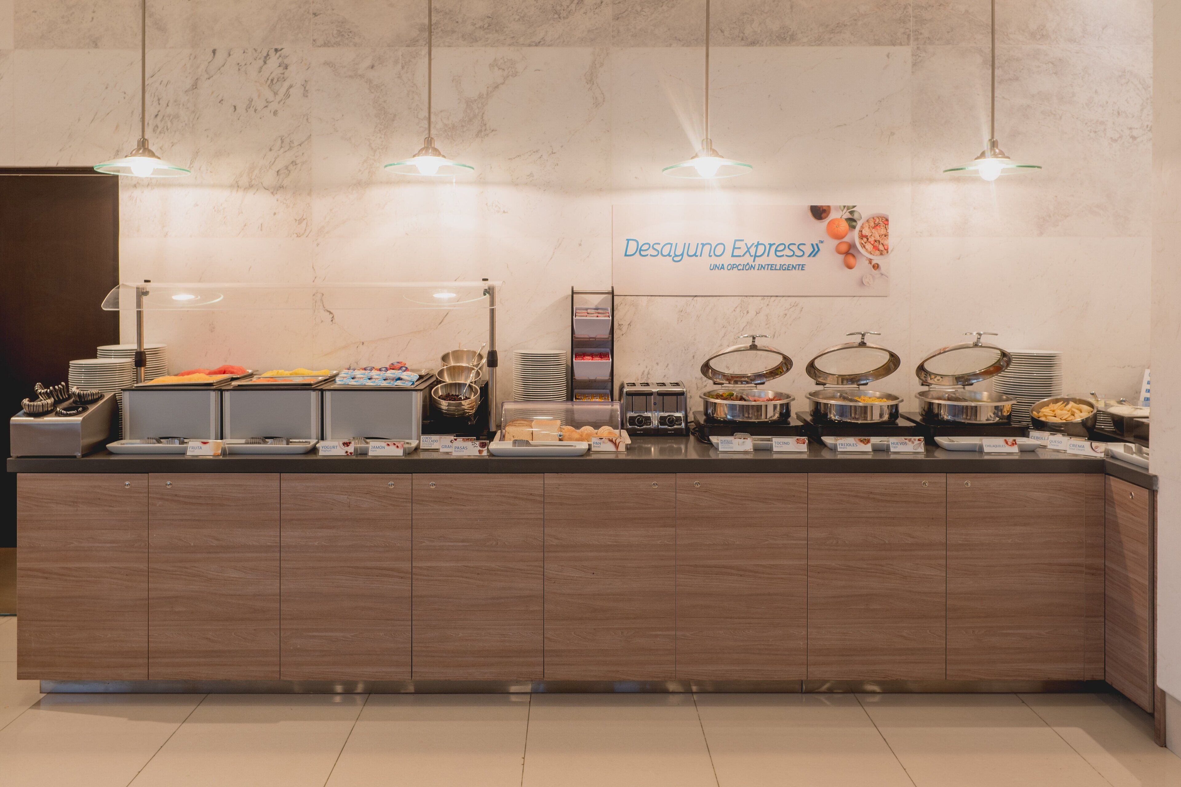Un banco buffet con diversi cibi e un cartello che recita 'Desayuno Express'.