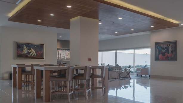 Un espace repas moderne avec un plafond en bois, de grandes fenêtres et des œuvres d’art accrochées aux murs.