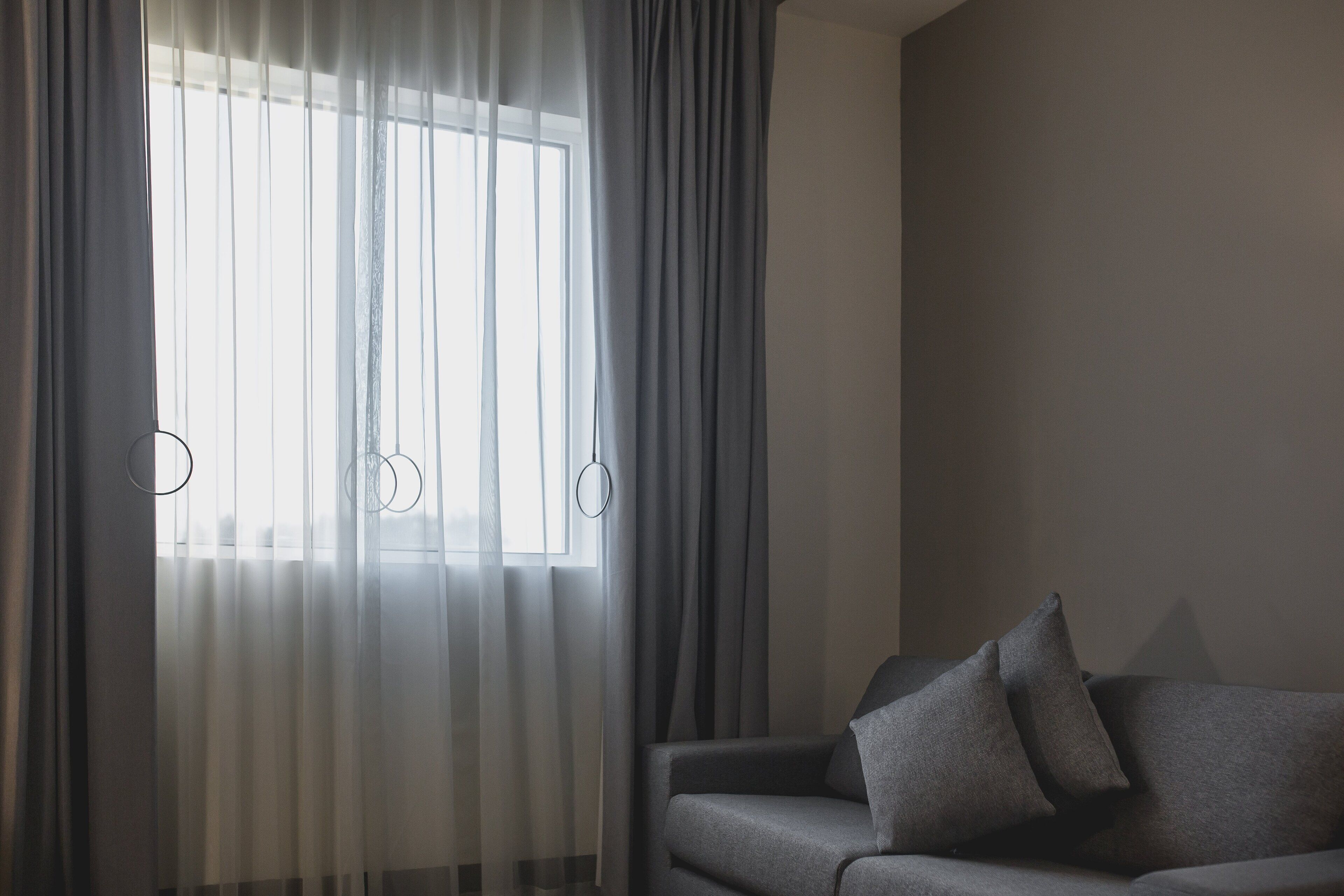 Una habitación con un sofá gris y una ventana con cortinas de tul.