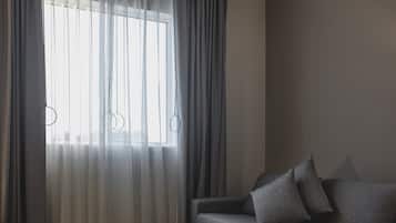 Una habitación con un sofá gris y una ventana con cortinas de tul.