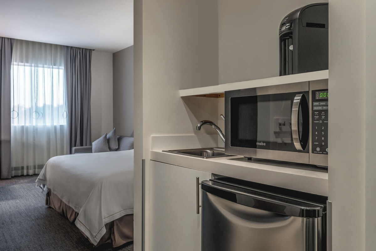 Une chambre d’hôtel comprenant un lit, une kitchenette équipée d’un four à micro-ondes, d’une machine à café et d’un réfrigérateur.