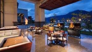 An outdoor patio area with seating, a grill, and a view of mountains. - Hilton Linzhi Resort (Nyingtri)