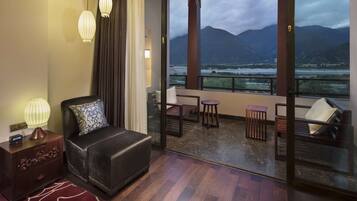 Relax in a stylish room with a large bed, nightstand, and balcony overlooking scenic mountains and a river.