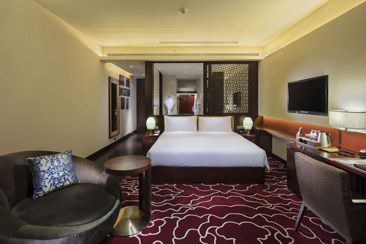 A hotel room with a large bed, a desk with a chair, a sofa, and a small round table.