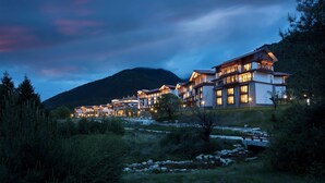 A resort with multiple buildings, a mountain backdrop, and a stream in the foreground. - Hilton Linzhi Resort (Nyingtri)