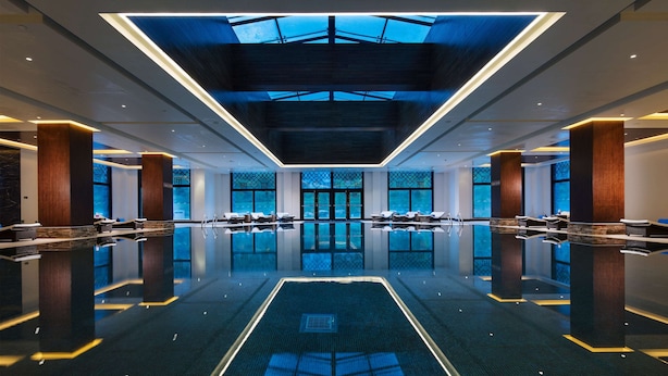 A modern hotel lobby with a central swimming pool, large windows, and a high ceiling with skylights. - Hilton Linzhi Resort (Nyingtri)