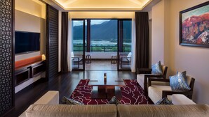 A modern living room with a large TV, comfortable seating, a coffee table, and a scenic mountain view through large windows. - Hilton Linzhi Resort (Nyingtri)