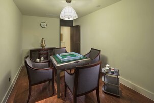 Un comedor con una mesa dispuesta para cuatro personas, sillas, una mesita auxiliar con una tetera y un reloj en la pared.
