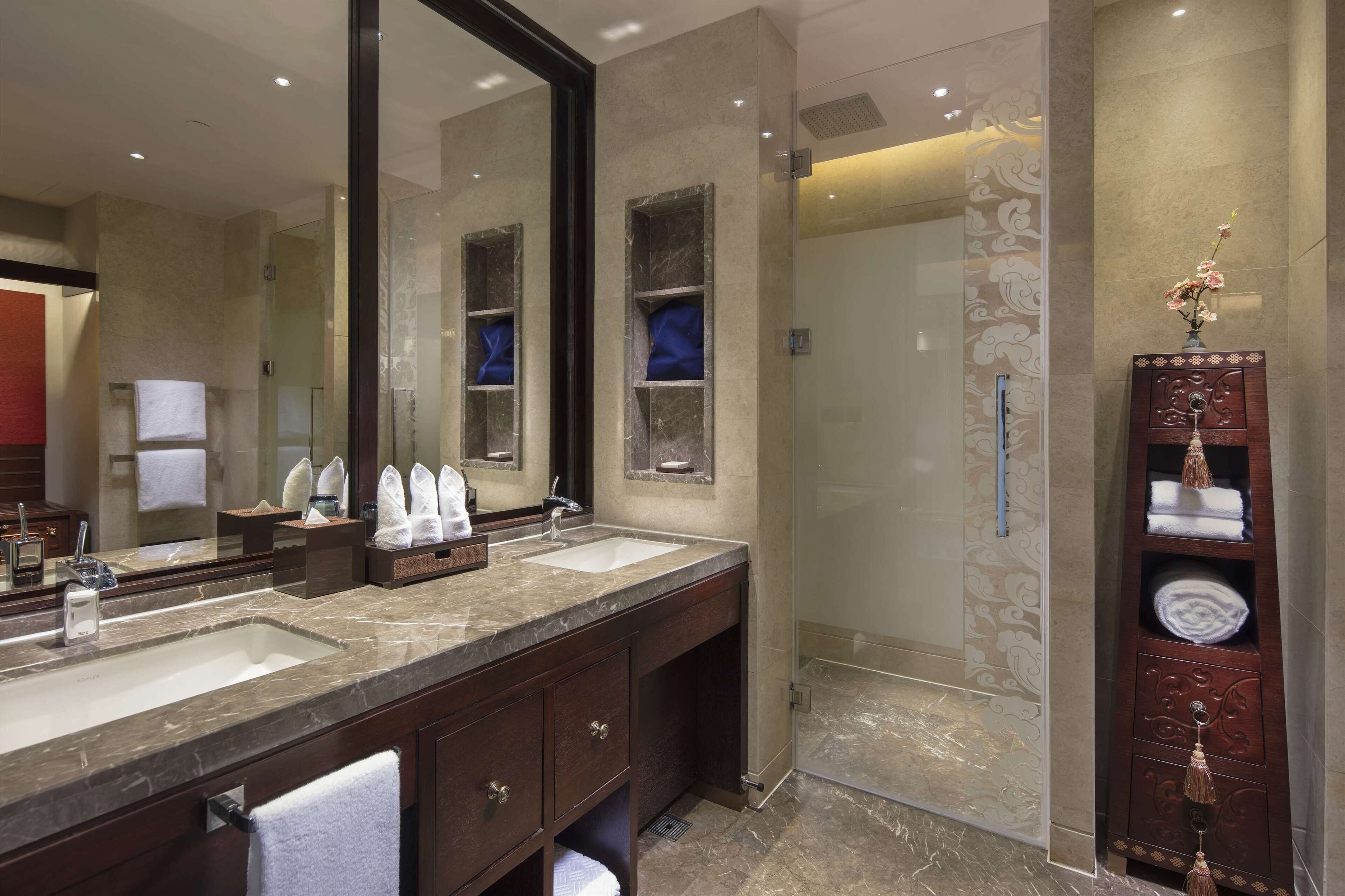 A modern bathroom with two sinks, a large mirror, and a walk-in shower.