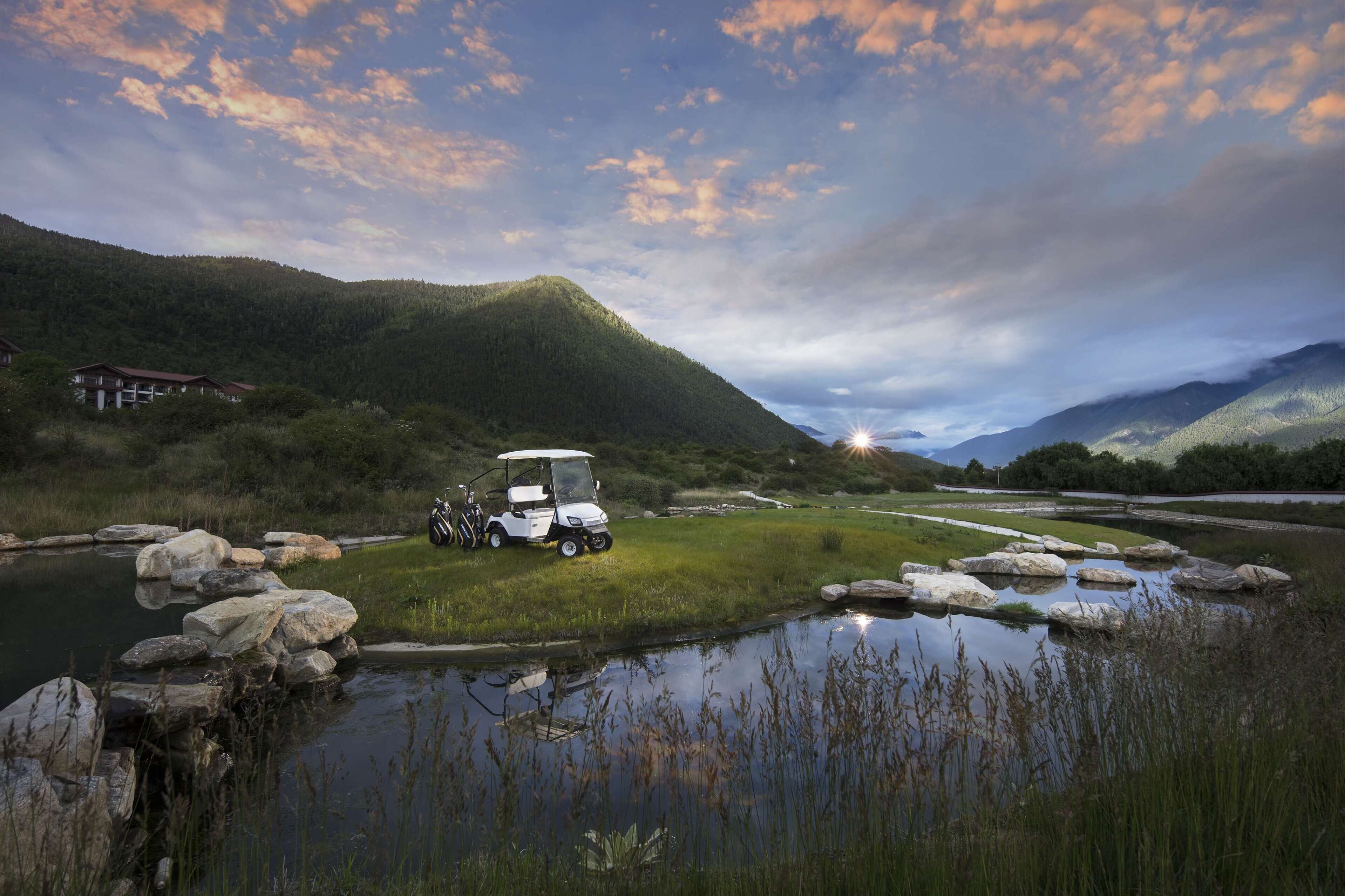 Un carrito de golf estacionado junto a un lago tranquilo, con montañas al fondo.