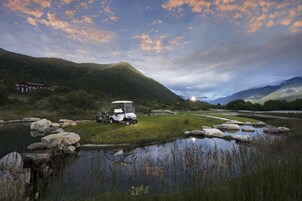 Un carrito de golf estacionado junto a un lago tranquilo, con montañas al fondo.
