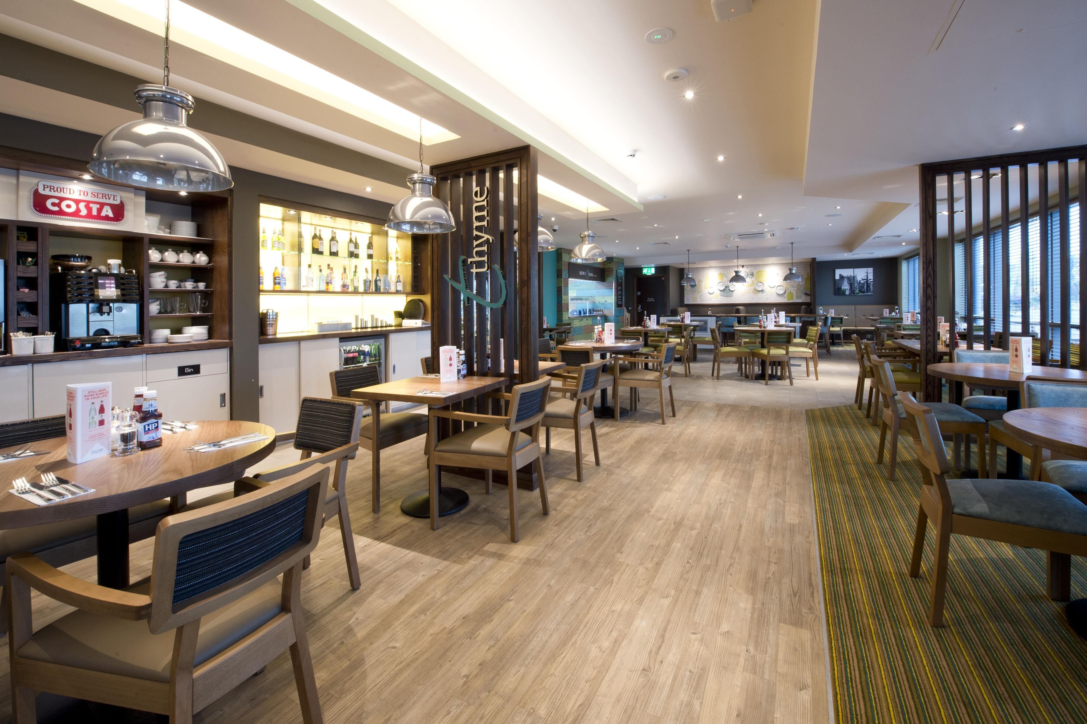 A modern restaurant with wooden tables and chairs, a bar area, and a view of the city.