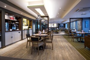 Un restaurante moderno con mobiliario de madera, una zona de bar y un área de comedor con mesas y sillas.