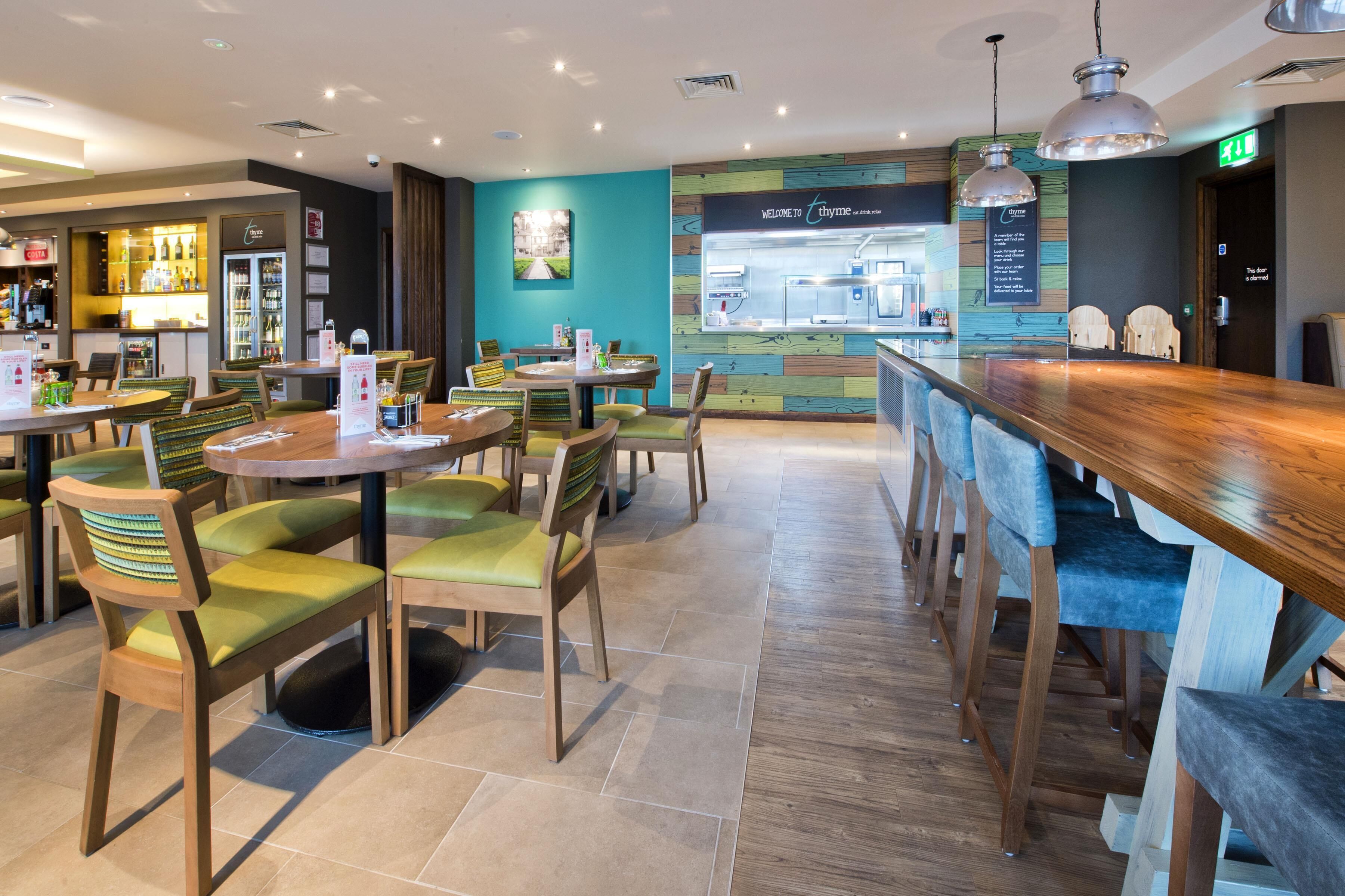 A restaurant with multiple tables and chairs, a bar area, and a kitchen visible through a glass partition.