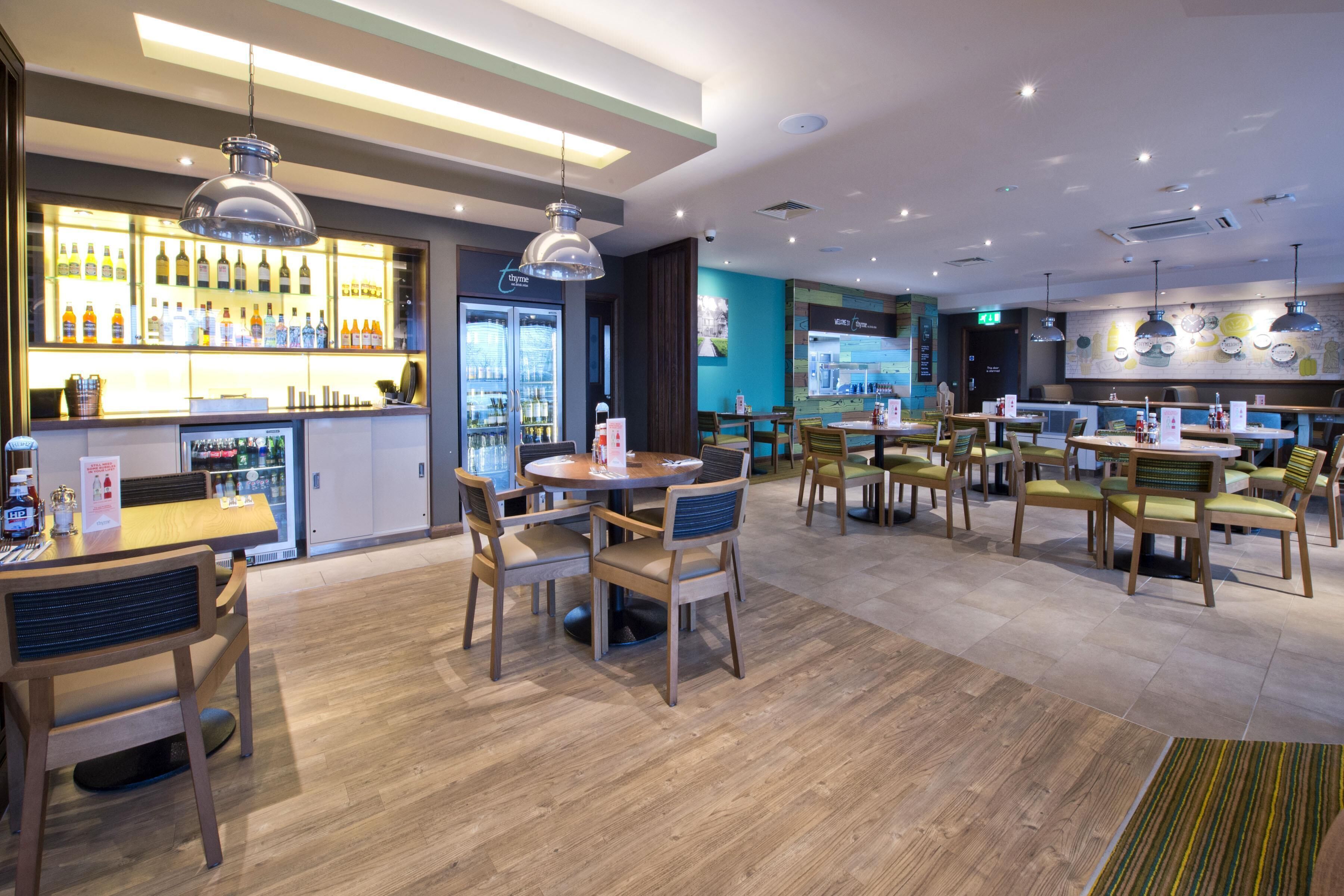 Ein modernes Restaurant mit Holztischen und -stühlen, einer Bar mit Flaschen sowie einer blauen Wand mit einer Karte.