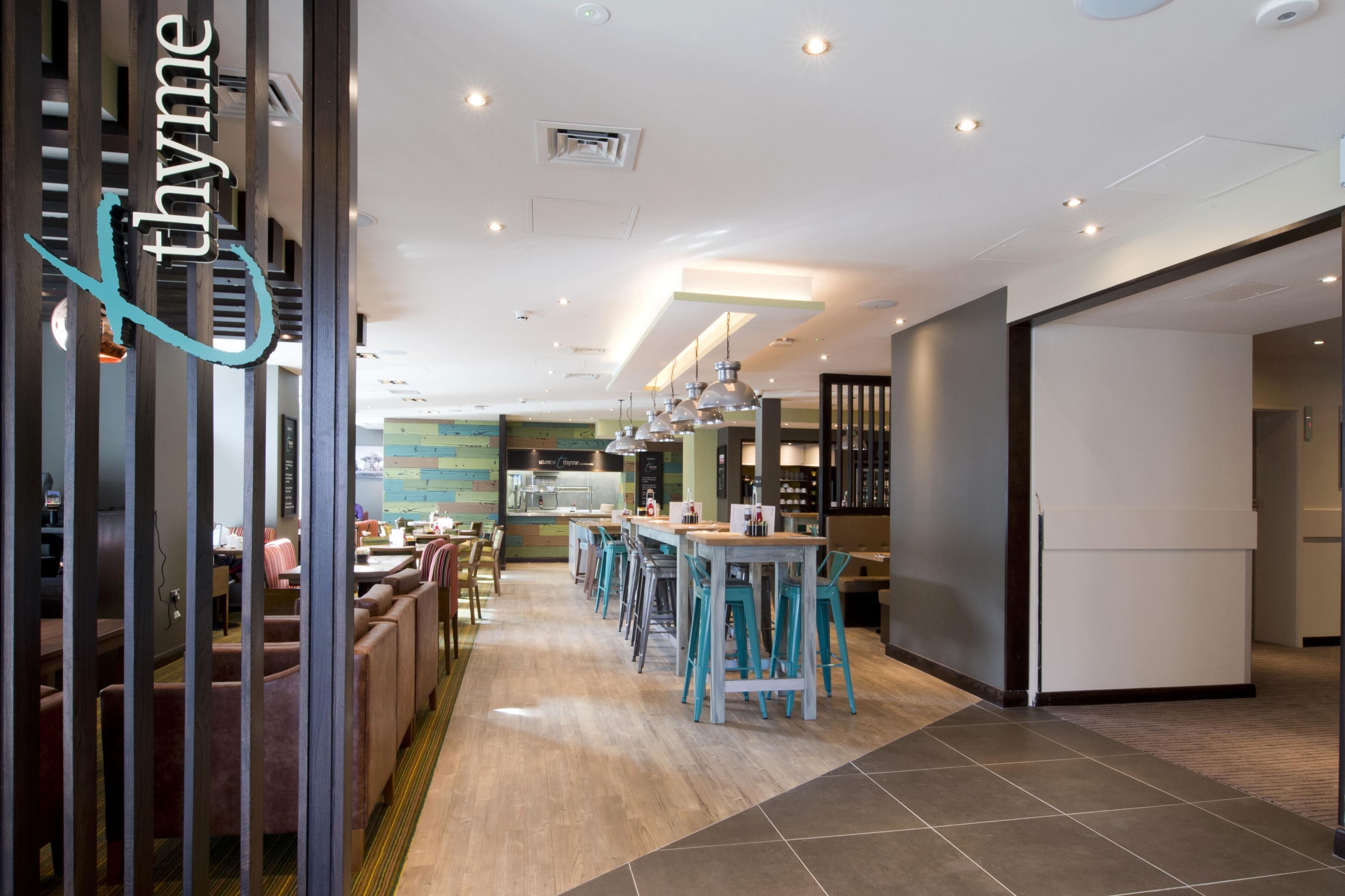 A modern restaurant with a long counter, multiple seating areas, and a visible kitchen area.
