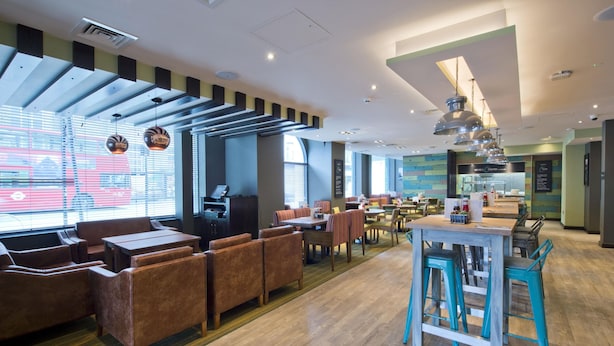 A modern restaurant with wooden flooring, a variety of seating including booths and tables, and large windows allowing natural light. - Premier Inn London Clapham (London)