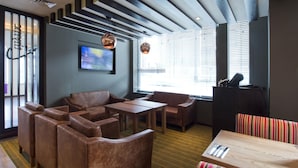 A modern lounge area with leather sofas, a wooden table, and a television screen. - Premier Inn London Clapham (London)