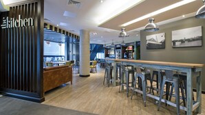 Un espace bar moderne avec des tabourets, un comptoir en bois et une enseigne indiquant « la cuisine ».