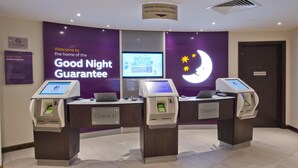 En hotellreception med tre incheckningskiosker, en digital skärm som visar menyn och en skylt som anger en snabbare utlämning av nycklar för gäster som har checkat in online.