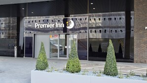 Fasaden på ett Premier Inn-hotell, med en modern design, stora glasfönster och tre välklippta, konformade prydnadsbuskar framför.