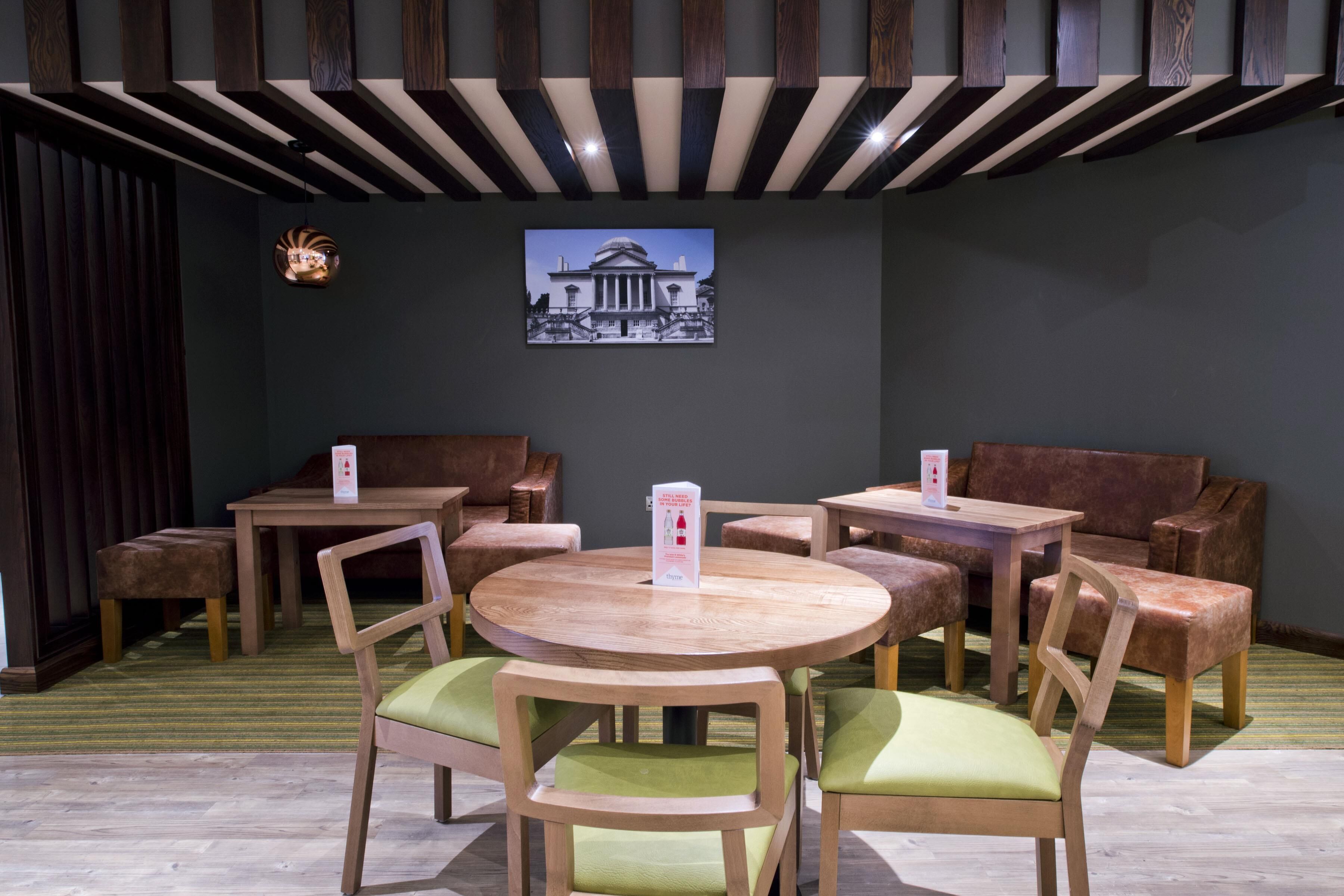 Interior de restaurante con mesas redondas, sillas acolchadas y un cuadro colgado en la pared.