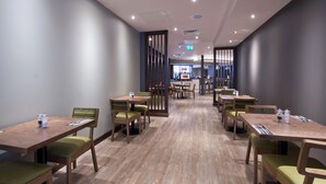 En restaurang med träbord och stolar, en central gångväg och en bardisk i bakgrunden.