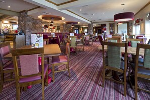 Un restaurant avec des tables et des chaises en bois, une moquette à motifs et un pilier en briques.