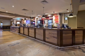 Una zona de bar con una barra larga, varios dispensadores de bebidas e iluminación colgante.