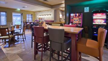 A restaurant with a bar area, tables, chairs, and slot machines.