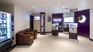 L’espace d’accueil d’un hôtel Premier Inn est équipé d’un terminal en libre-service, d’un écran de télévision, d’un distributeur automatique et de sièges.