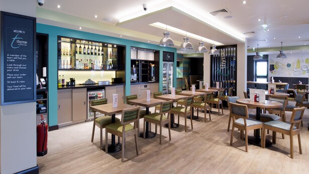 Un restaurant avec des tables et des chaises en bois, un coin bar et un tableau affichant le menu.