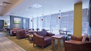 A hotel lobby with leather sofas, wooden tables, and large windows with blinds. - Premier Inn Slough Central South (Slough)