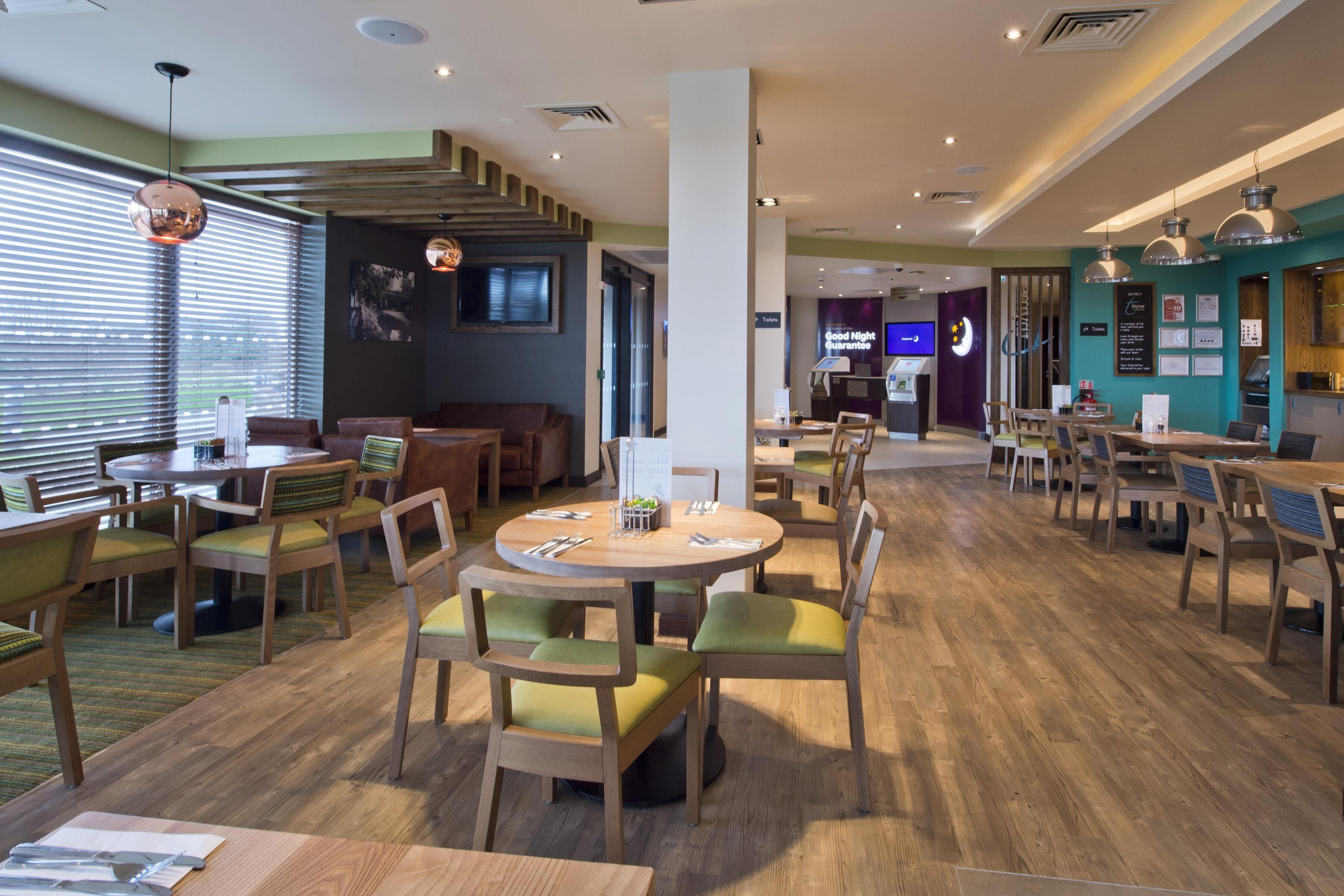 Un restaurant moderne avec des tables rondes, des chaises rembourrées de tissu vert et un plancher en bois.