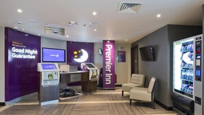 Rebedor d'hotel amb taulell de recepció, una caixa d'autoinformació, un cartell de Premier Inn, zona de seients i màquina expenedora.