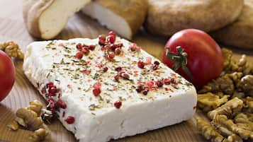 A block of cheese garnished with herbs and berries, surrounded by walnuts and tomatoes on a wooden surface.