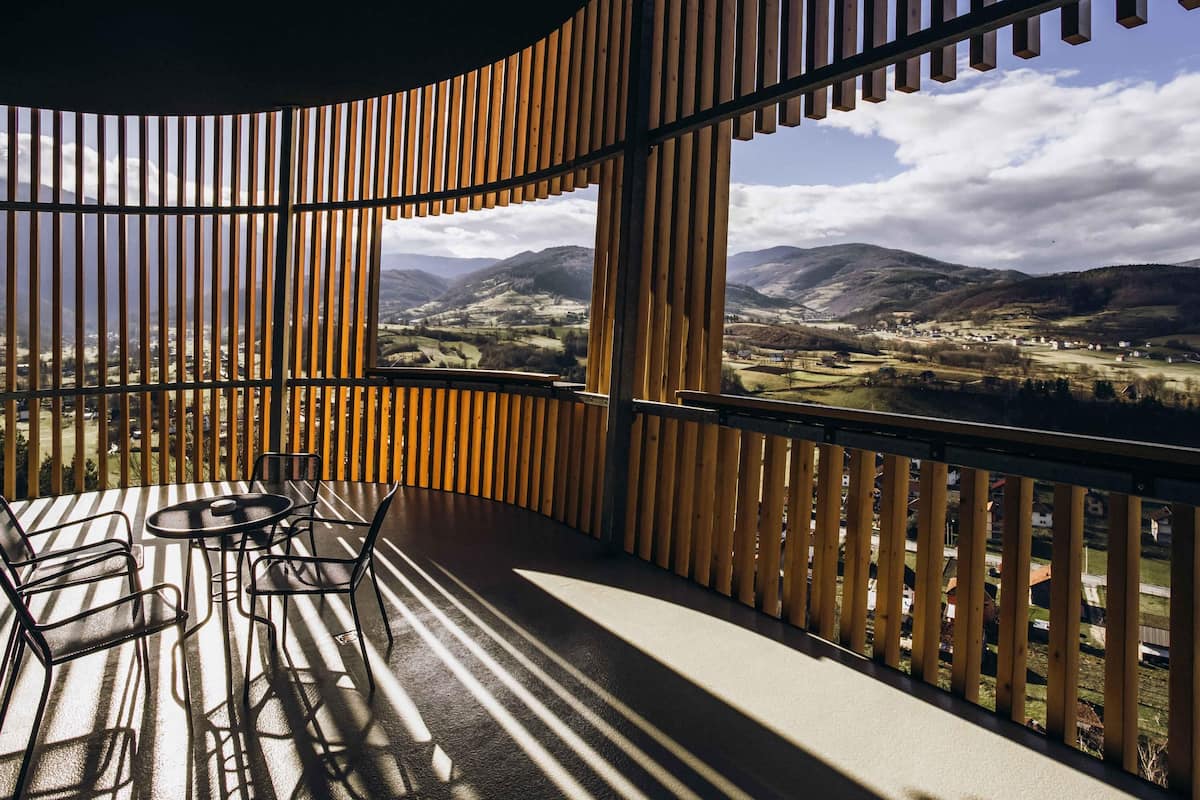 A balcony with a view of a valley, wooden slats, and a table with chairs.